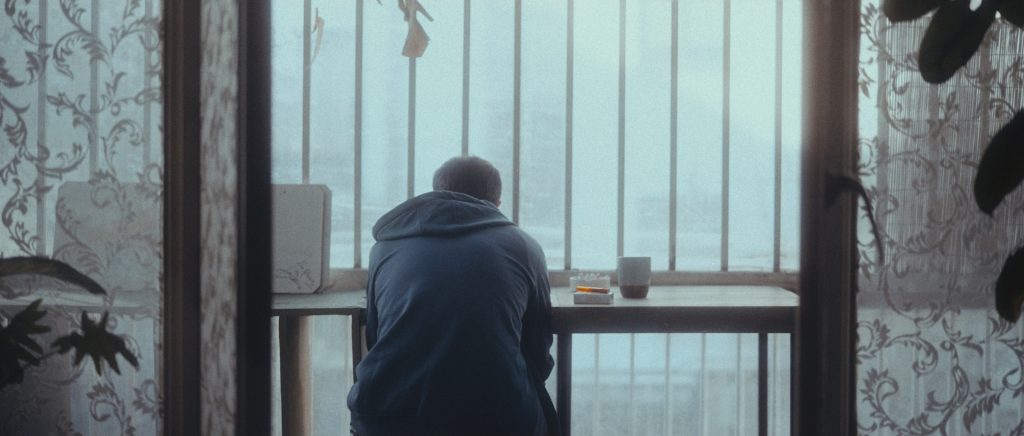A still from an independent film distributed by Pyramoon, showing a boy sitting in the balcony