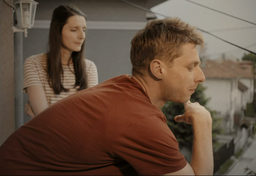 A young couple standing on a balcony, looking down pensively – from the film "Good Luck Sara!"