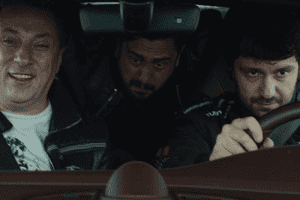 Three men sitting in a car, two of them look excited about the high speed and the other one looks scared