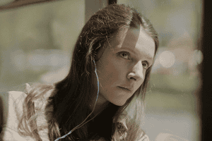 Sara sitting alone on a bus with her head against the window, listening to music with headphones on.