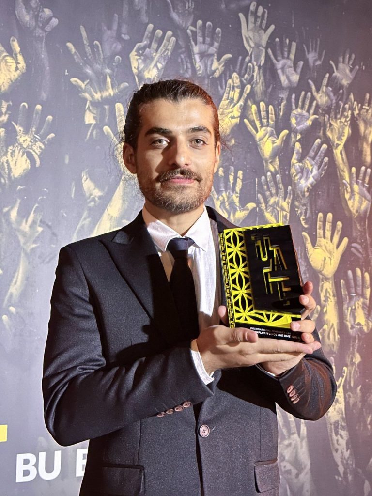 Moein Rahmanzadeh holding Best Screenplay award at UAFF
